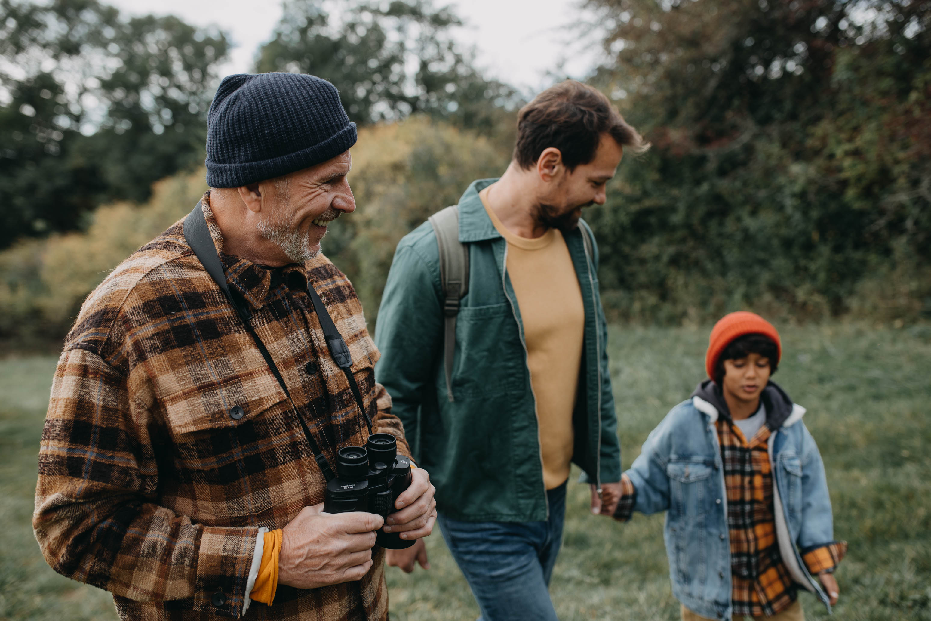 A small multiracial boy with father and grandfather walking in forest nature in autumn day