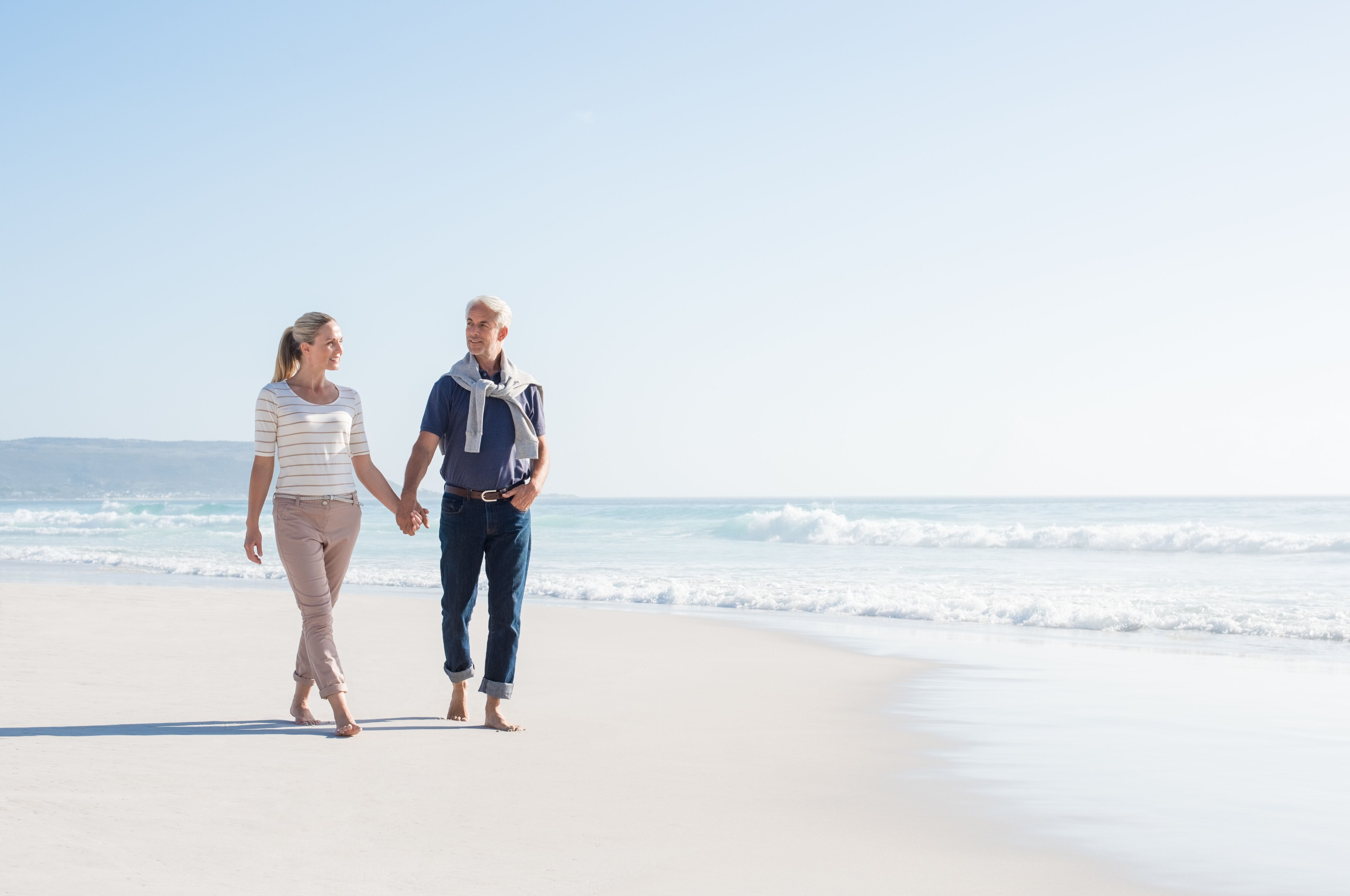 Senior couple holding hands at the beach on a sunny day.