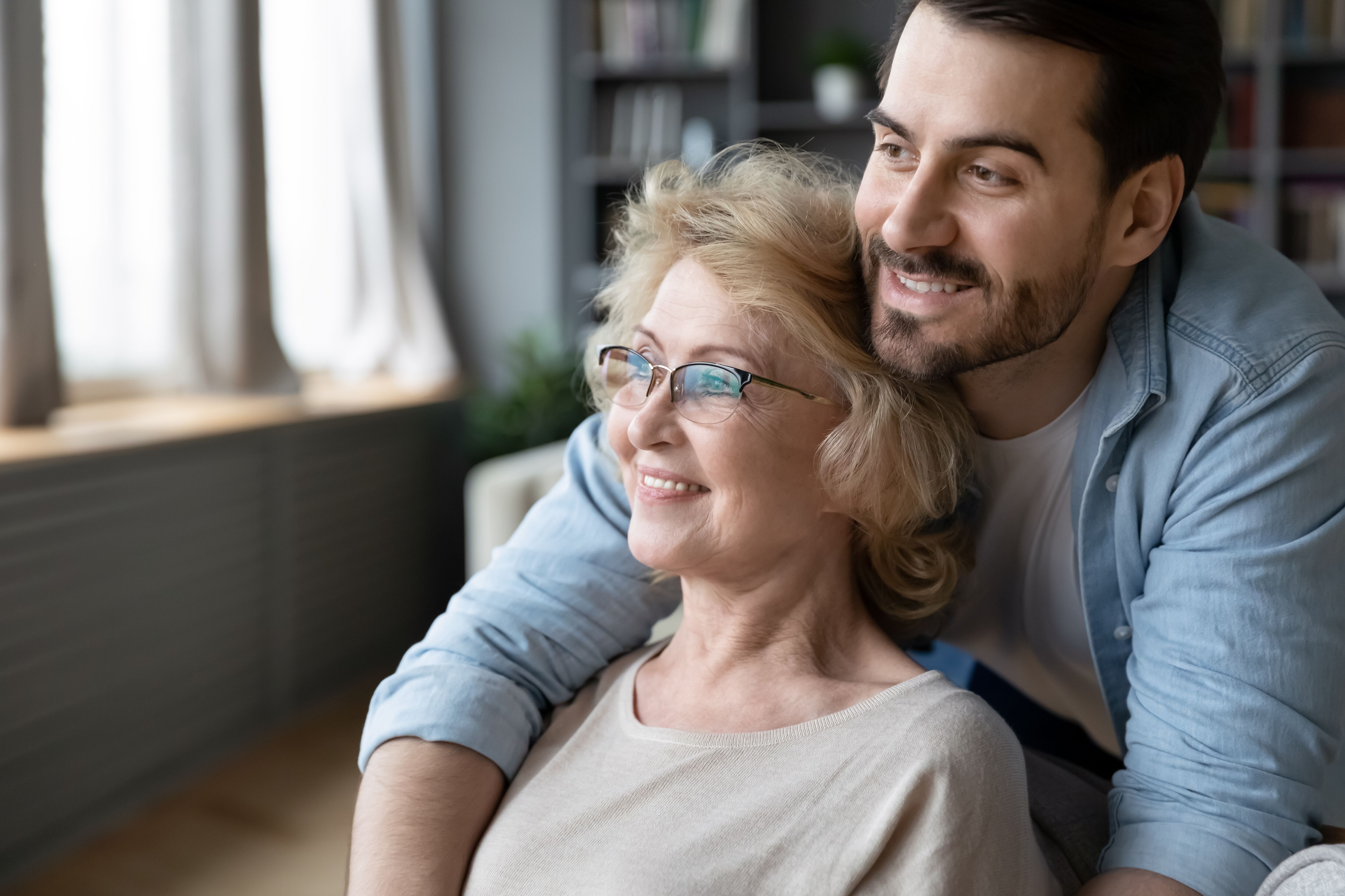 Happy hopeful middle-aged mother and adult son hug look in window