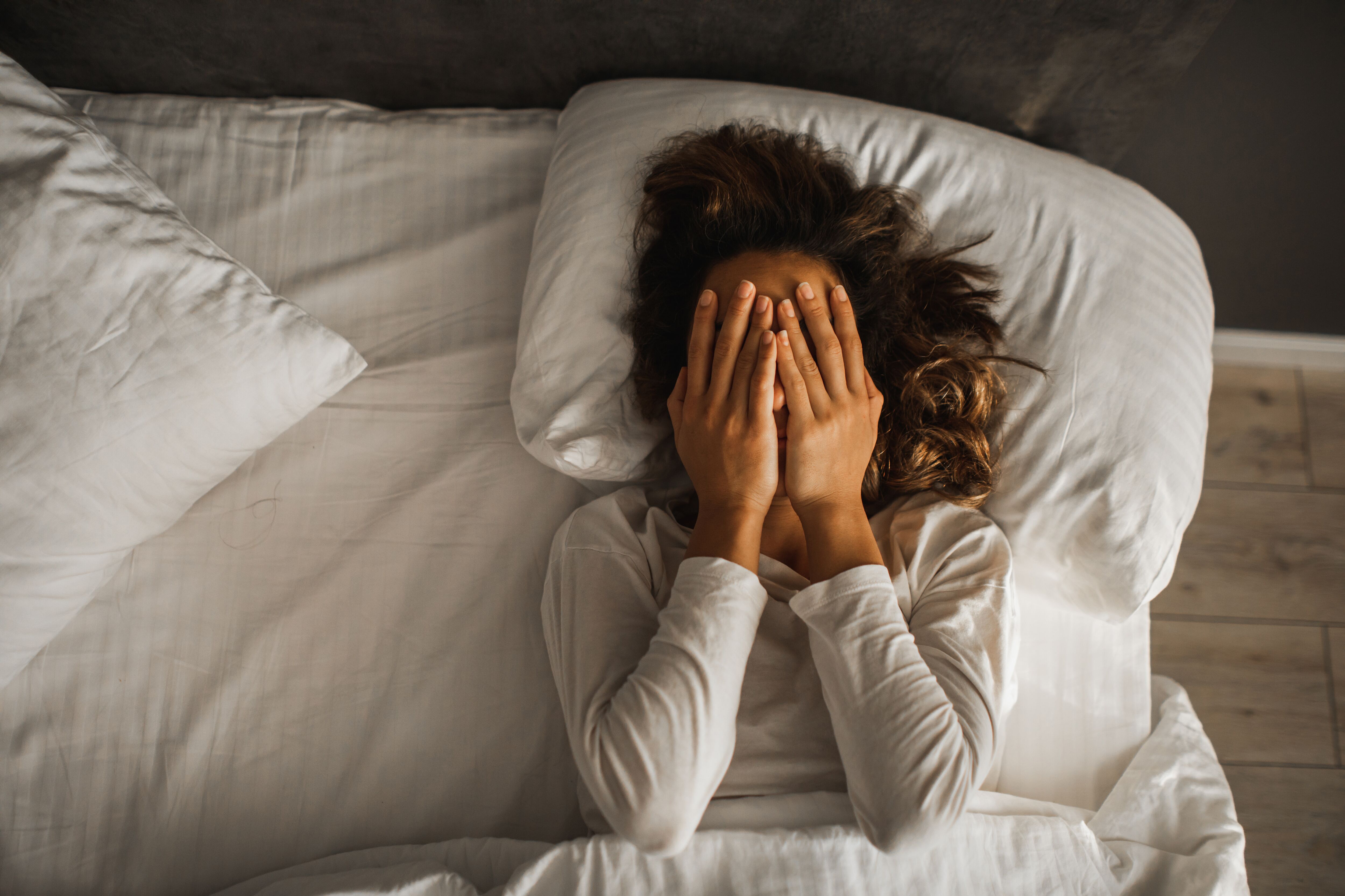Woman in depression closed face with hands and crying in bed.