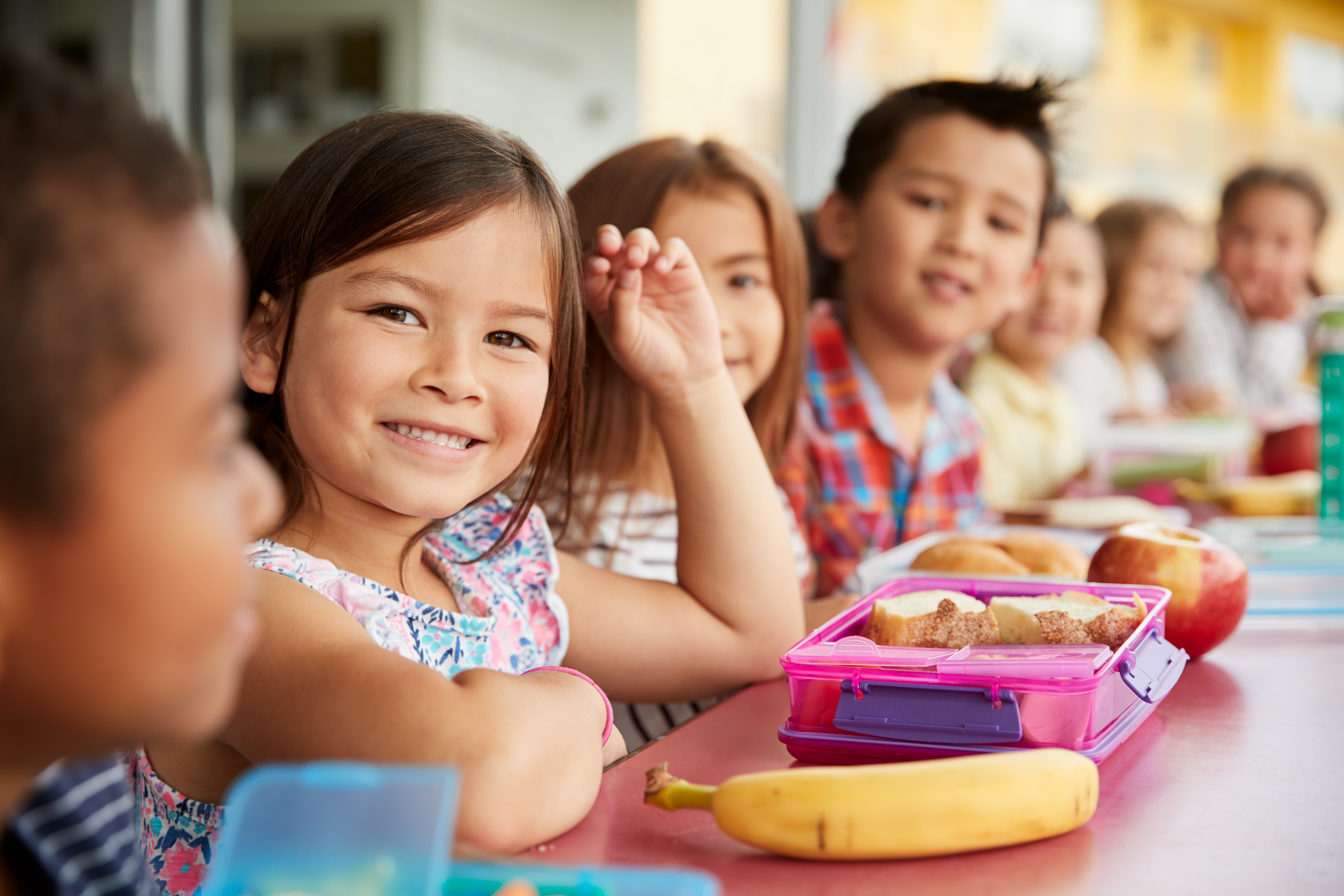 Elementary school kids sitting a table with packed lunches